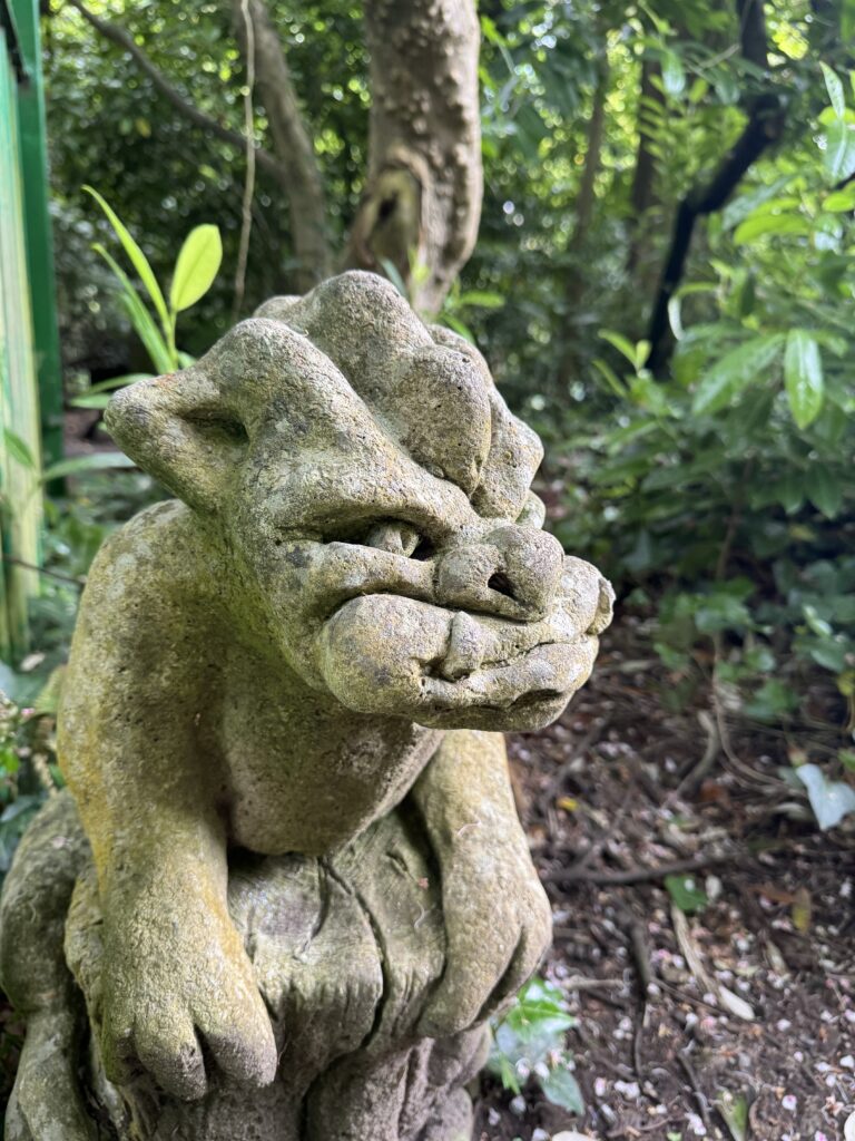 A picture of an ugly gargoyle with leaves and small tress in the background.