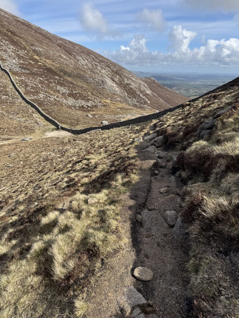 A narrow mountain path descending towards the Mourne Wall in the Mourne Mountains.