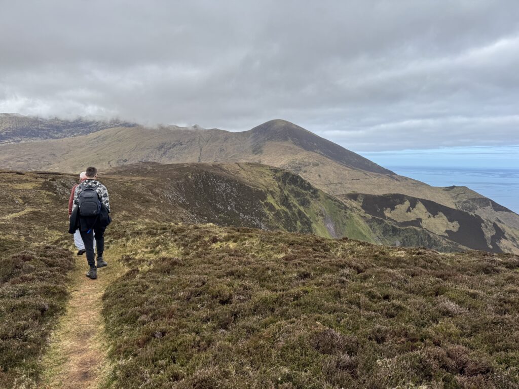 Hikers walking through heather towards the rugged mountain slopes above Sauce Creek on the Dingle Peninsula.