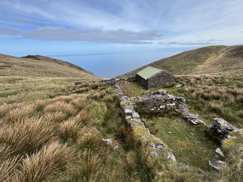 Old stone building with a green roof on the Masatiompan and Sauce Creek walk, surrounded by mountain slopes with the Atlantic Ocean beyond.