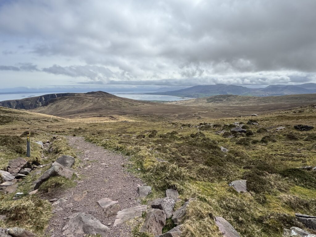 Mountain trail overlooking Brandon Bay and the surrounding mountains beneath dramatic clouds on the Dingle Peninsula.