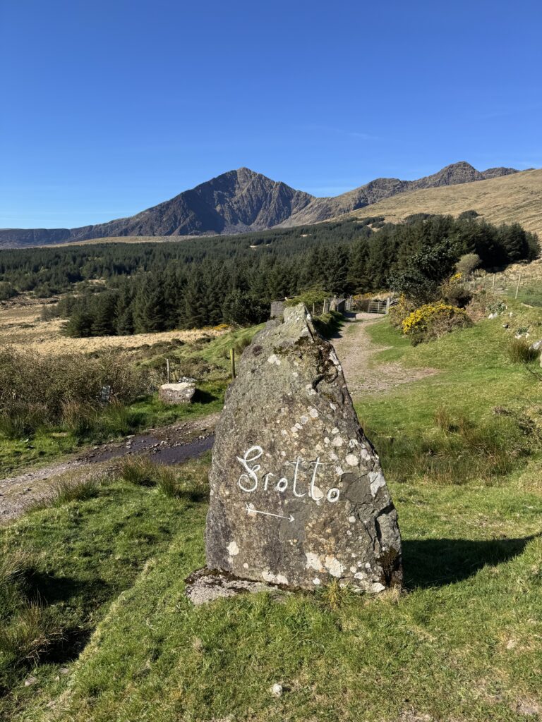 Mount Brandon Loop trail near Cloghane, with a stone marker pointing towards the Faha Grotto and the Brandon Mountains behind.