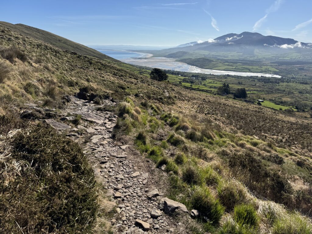Rocky path on the Mount Brandon Loop overlooking Brandon Bay, with green farmland, tidal flats and mountains in the distance