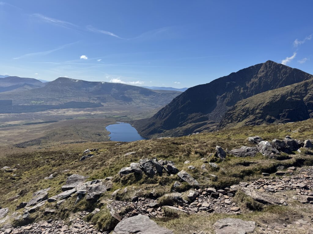 Mountain lake surrounded by steep rocky cliffs and open moorland along the Faha Route towards Mount Brandon.