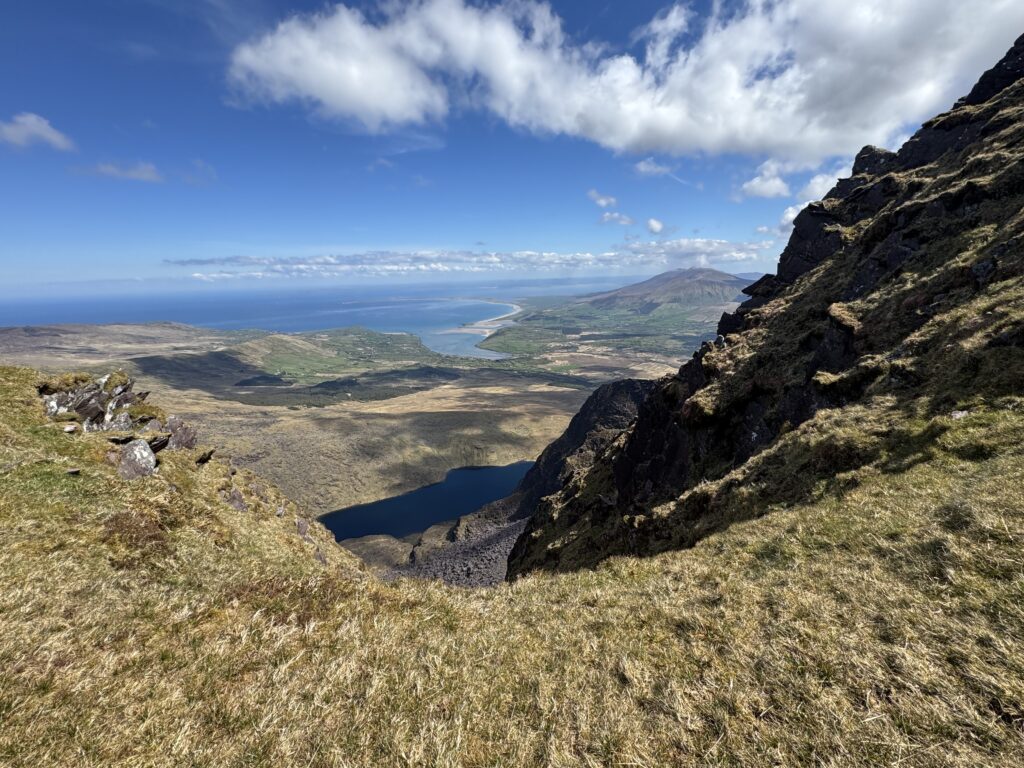 View from the Mount Brandon Loop down through the steep mountain cliffs towards a corrie lake and Brandon Bay.