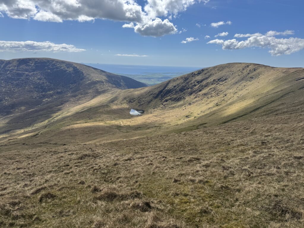 Mountain valley and small lake on the Mount Brandon Loop, with the Atlantic Ocean visible beyond the surrounding ridges.
