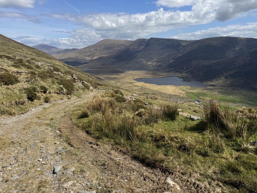 Rocky track descending on the Mount Brandon Loop towards a mountain lake surrounded by the slopes of the Brandon range.