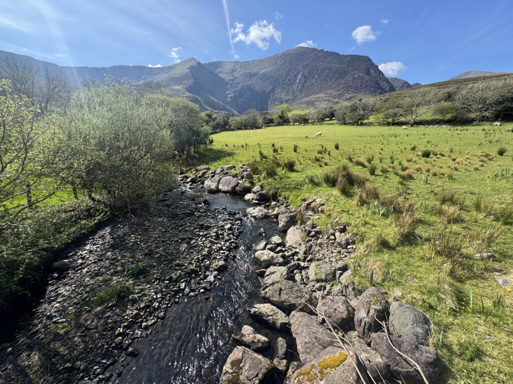 Mountain stream and green fields beneath the dramatic slopes of the Mount Brandon Loop near Cloghane.