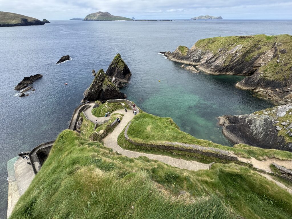 Spectacular views of Dunquin Pier, featured in our guide to the best walks in Dingle, showing the winding stone pathway descending towards turquoise Atlantic waters, surrounded by rugged cliffs and the Blasket Islands in the distance.