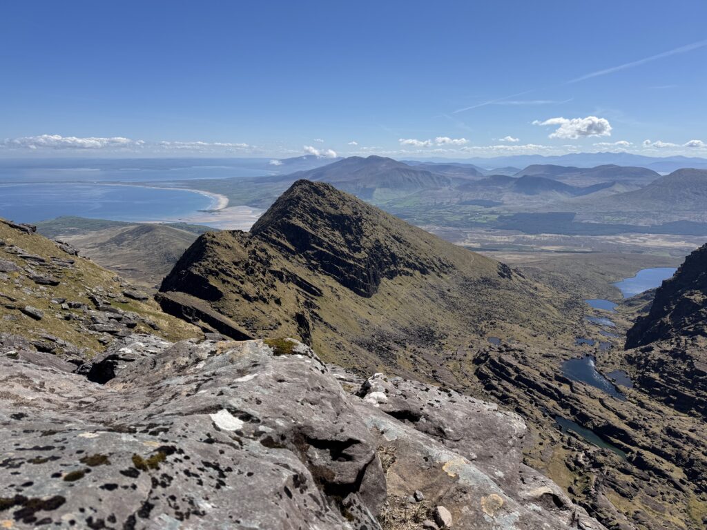 Spectacular views from Mount Brandon, one of the best walks in Dingle, overlooking rugged mountain ridges, glacial lakes and the sweeping Atlantic coastline beneath a clear blue sky.