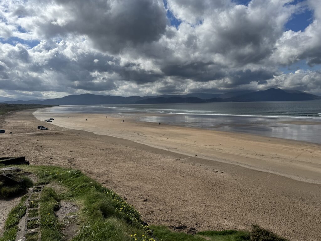 Inch Beach, one of the best walks in Dingle, with a vast stretch of golden sand, gentle Atlantic waves and distant mountains beneath dramatic grey clouds.