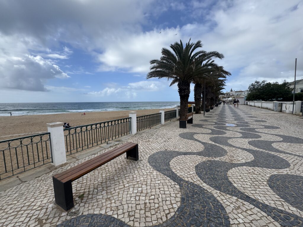 Palm tree-lined promenade overlooking the sandy beach and Atlantic Ocean at Praia da Luz, with decorative wave-patterned paving during our week in the Algarve with a 3 year old.