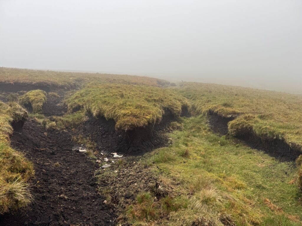 Eroded peat and boggy ground on the Lyracappul Loop, with deep muddy channels cutting through the grassy mountainside in thick mist.