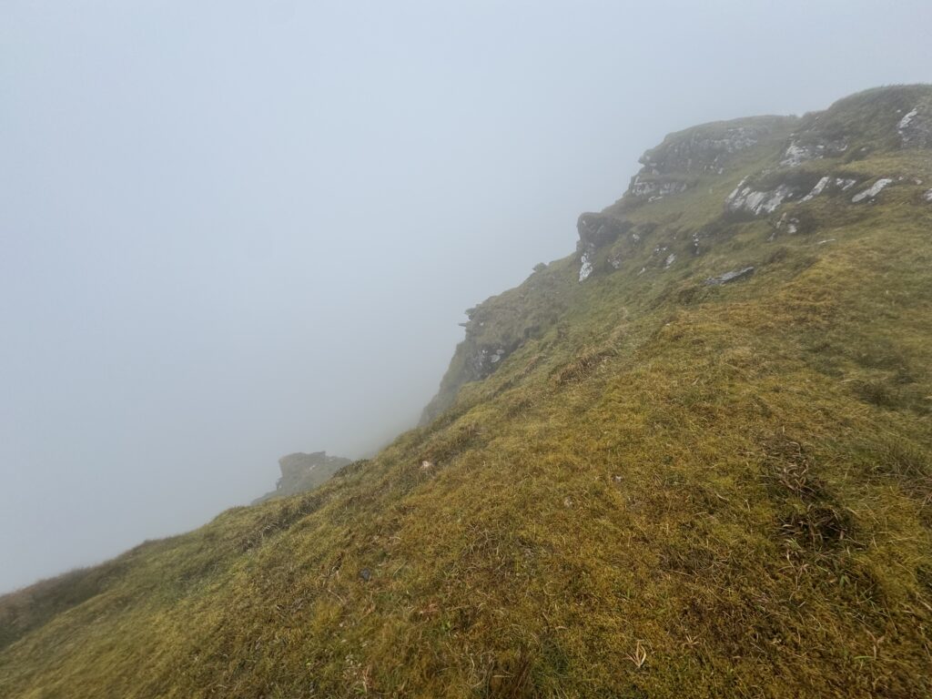 Rocky mountain ridge emerging from low cloud, with steep grassy slopes and rugged outcrops fading into mist in the Galtees.