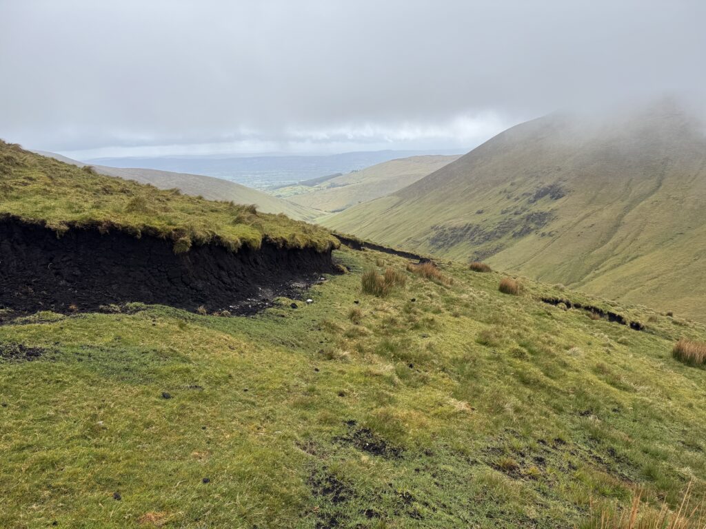 View from the Lyracappul Loop as the cloud begins to lift, revealing a broad green valley, steep mountain slopes and eroded peat banks in the Galtee Mountains.